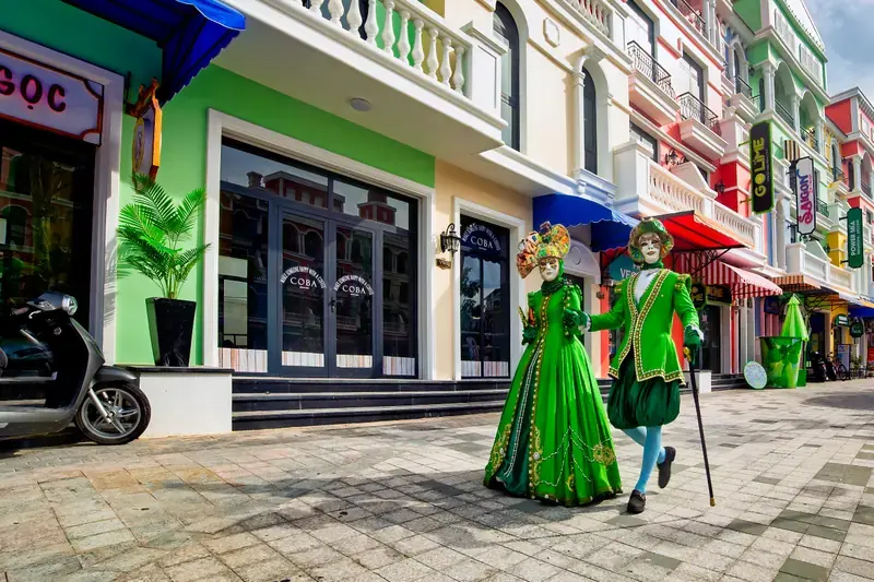 Two performers in green costumes walking past colourful Grand World shopfronts