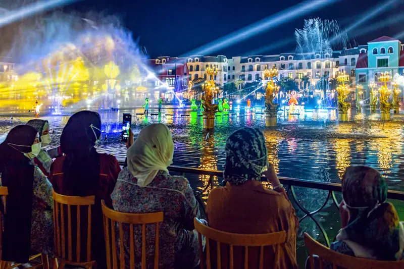 Visitors watching a waterside performance with fountains and lights at Grand World