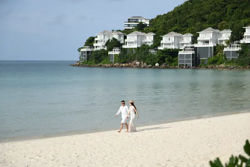 Couple walking on white sand at Khem Beach below hillside villas