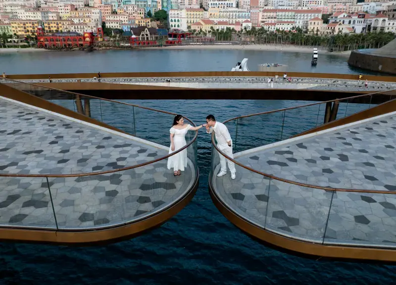 Couple in white posing on the two arms of Kiss Bridge with Sunset Town behind them