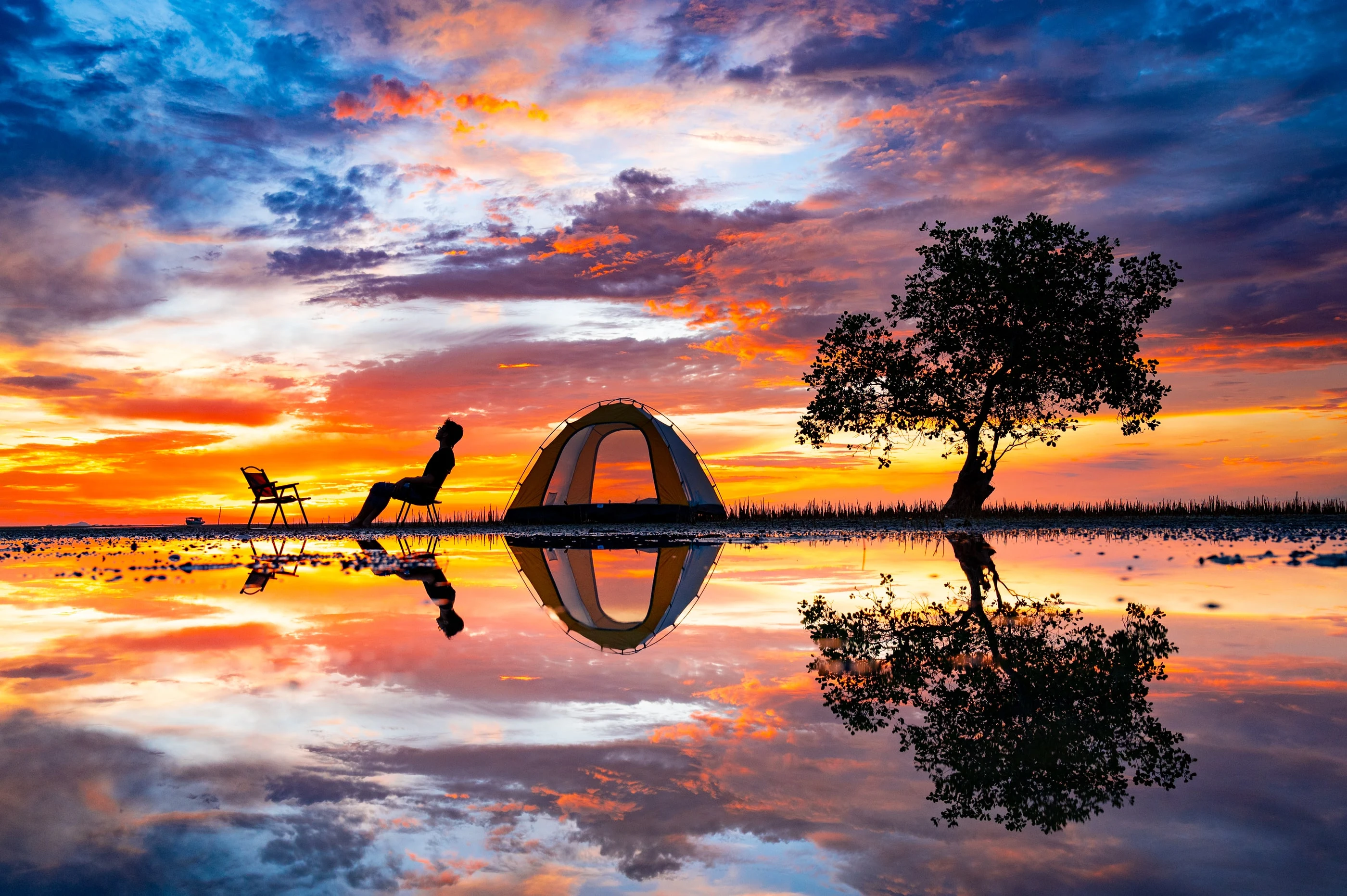 Người đàn ông ngồi cạnh lều và cây cô độc dưới bầu trời bình minh phản chiếu tại Phú Quốc