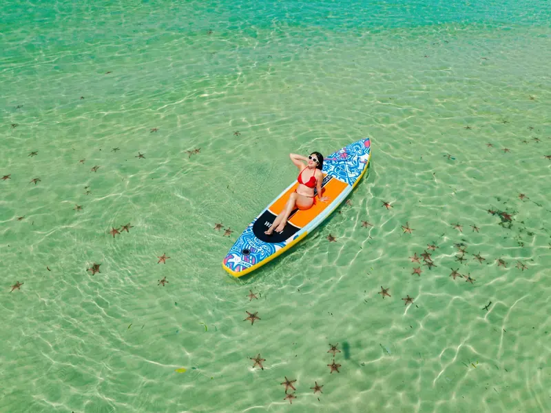 Aerial view of a traveller seated on a colourful paddleboard above shallow water