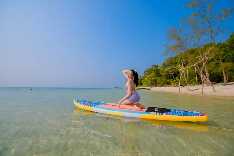 Traveller kneeling on a colourful paddleboard near a tree-lined beach