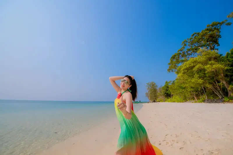 Traveller in a colourful dress on a sandy beach beside trees and the sea