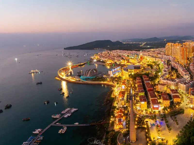 Aerial view of illuminated Sunset Town and Kiss Bridge beside the sea at dusk