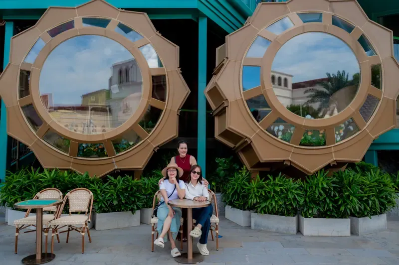 Ba người phụ nữ chụp ảnh cùng nhau bên bàn cà phê dưới những ô cửa tròn lớn.