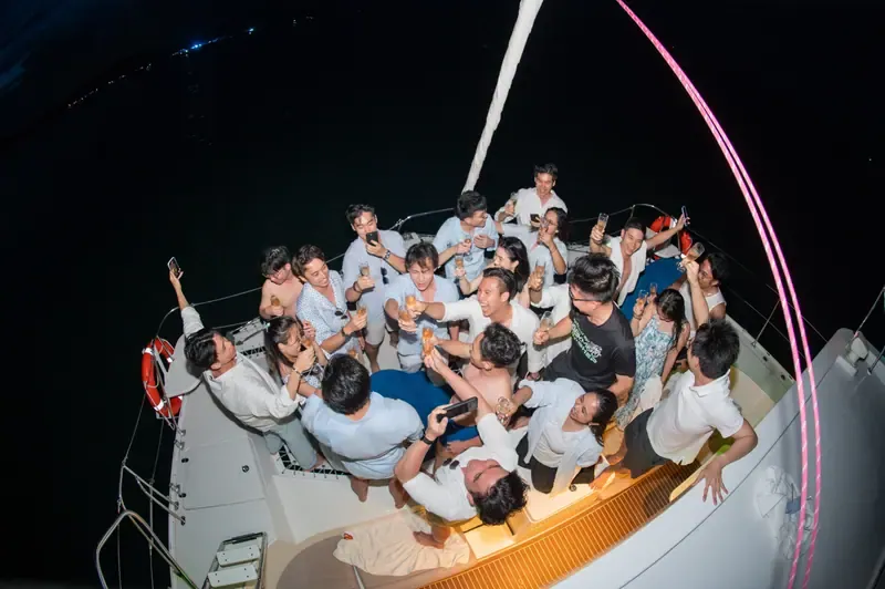 Guests raising glasses together on the deck of a catamaran at night, photographed from above.
