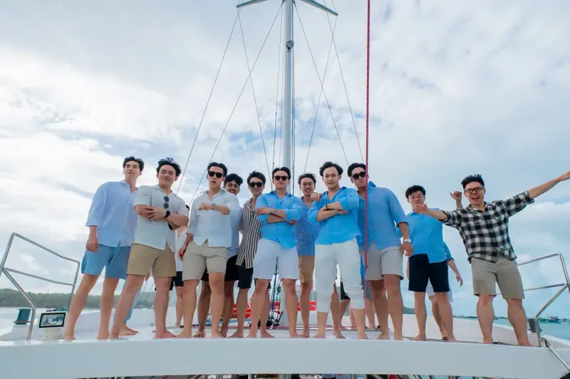 A group standing side by side on a boat deck beneath the mast, smiling and posing together.
